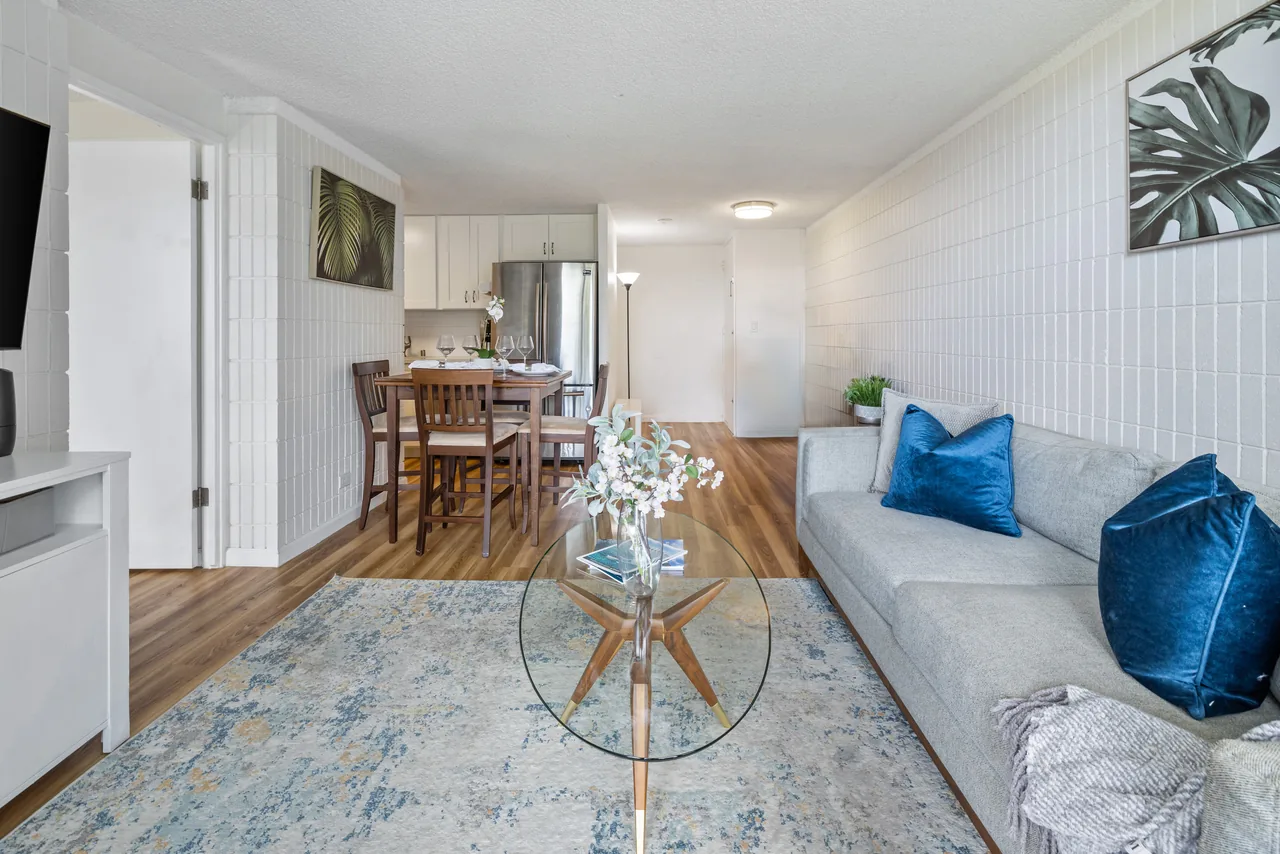Living room with a glass coffee table and sofa, looking through to the dining nook