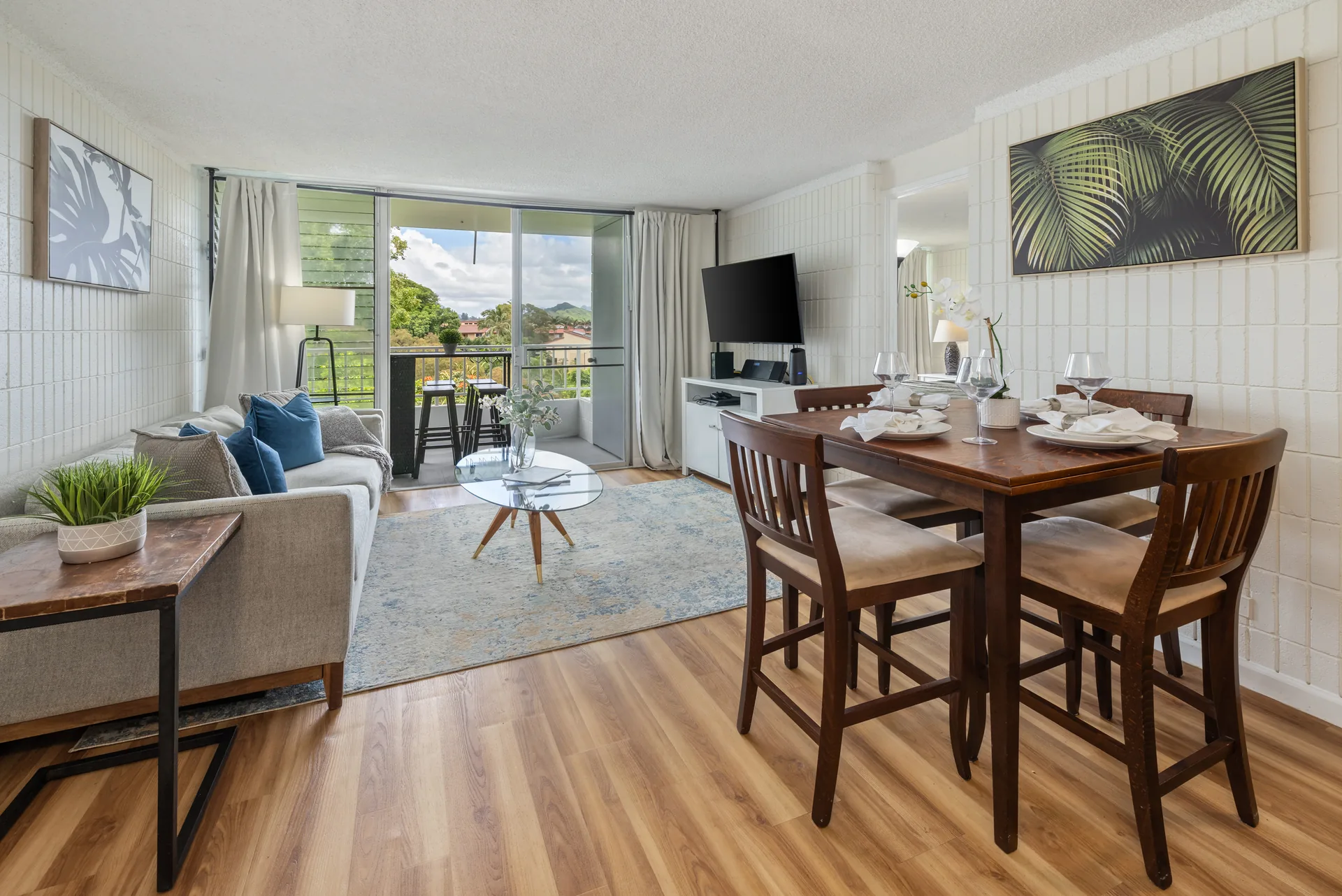 Bright, fully-furnished great room with lounge seating and a dining table beside windows framing the Koʻolau mountains